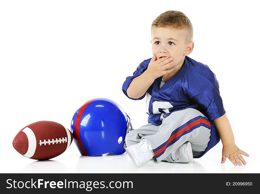 An adorable toddler in his football uniform covering his mouth in unbelief. His helmet and football sit by his side. Isolated on white. An adorable toddler in his football uniform covering his mouth in unbelief. His helmet and football sit by his side. Isolated on white.