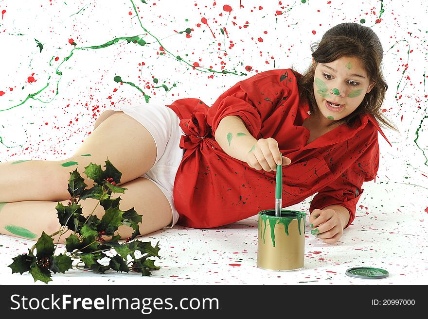 An attractive young teen dipping a paint brush into a bucket of geen paint, while surrounded and covered by Christmas-colored splatters. An attractive young teen dipping a paint brush into a bucket of geen paint, while surrounded and covered by Christmas-colored splatters.