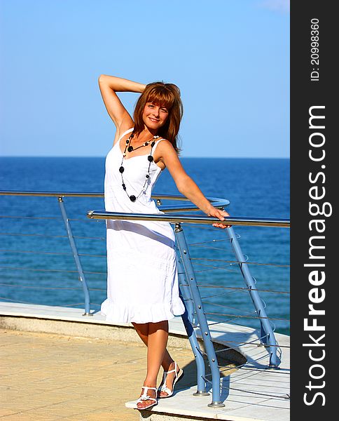 A beautiful woman on a balcony by the sea ( ocean) holding her hair  with blue sky background. A beautiful woman on a balcony by the sea ( ocean) holding her hair  with blue sky background