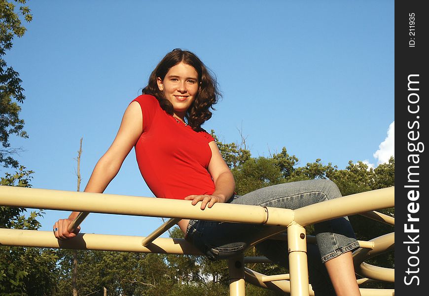 Teenage girl perched on playground monkey bars. Teenage girl perched on playground monkey bars