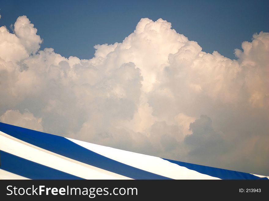 A blue and white stripped roof abstract against a blue and cotton candy clouds.