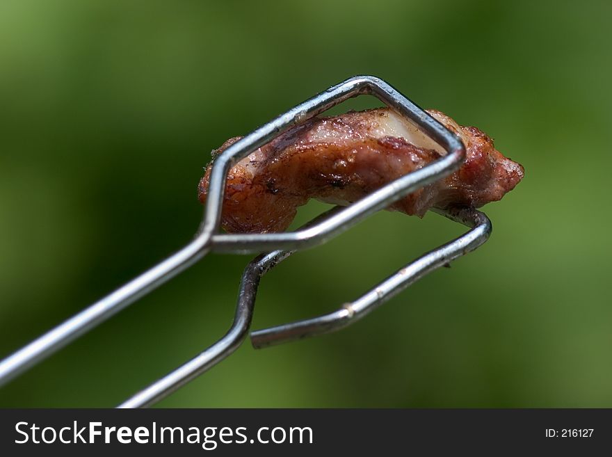 Pincers holding roasted meat over green background. Pincers holding roasted meat over green background