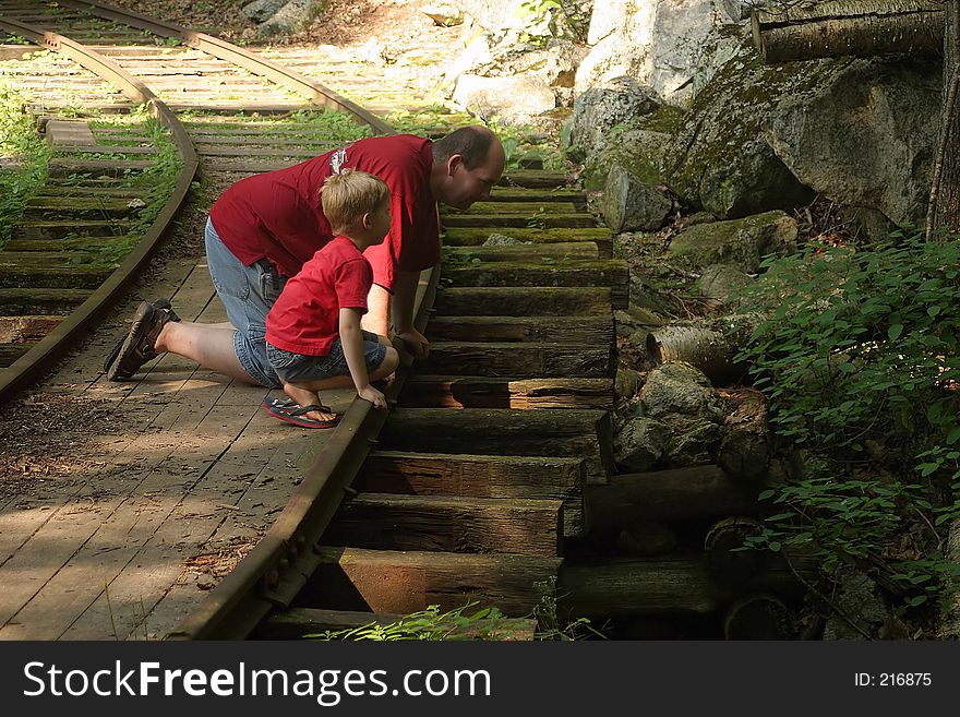 A father and son kneeling on an old railroad track. A father and son kneeling on an old railroad track.