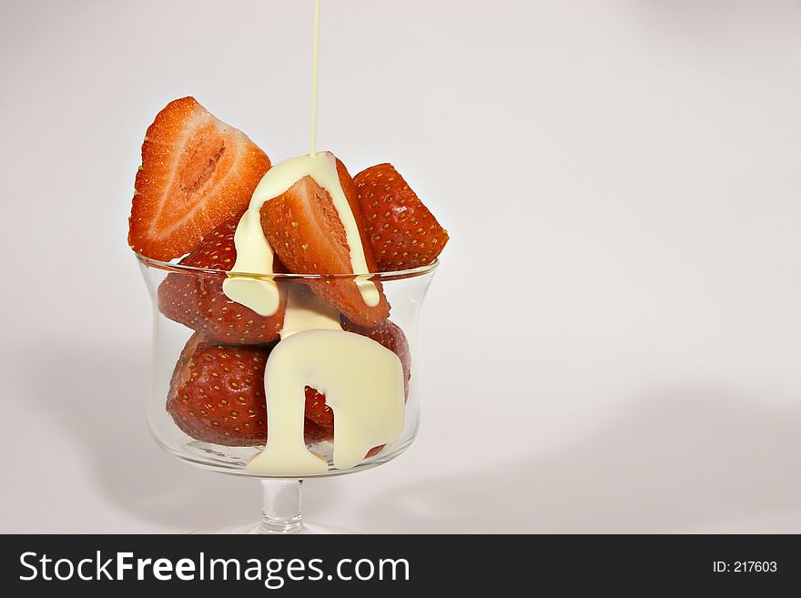 Pouring cream over a dessert glass full of ripe juicey strewberries. Pouring cream over a dessert glass full of ripe juicey strewberries.