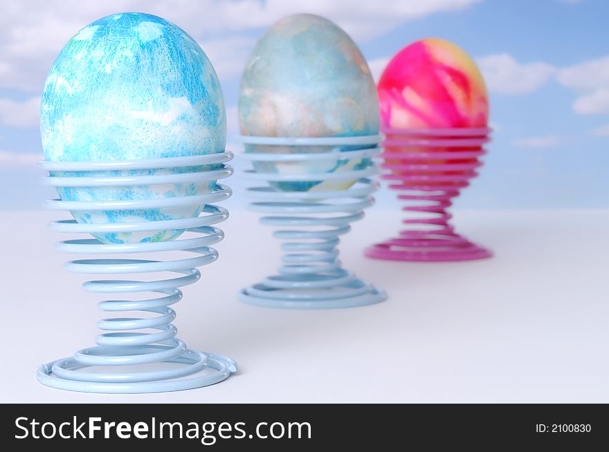 Three Decorated Easter Eggs on Coil Springs against a Blue Sky with Clouds