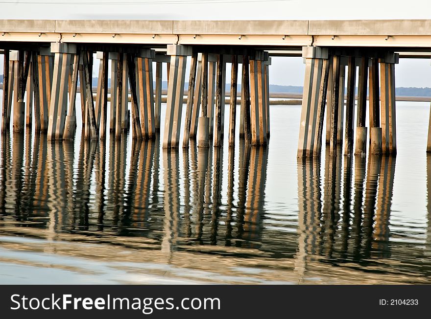 Bridge supports reflected in water with warm light from sunset