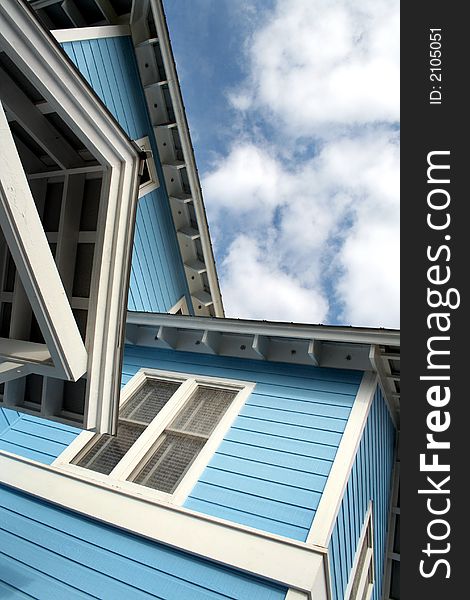 Upward view of corner of beach house against blue sky with white clouds. Upward view of corner of beach house against blue sky with white clouds