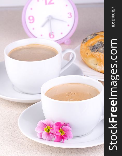 Two cups of coffee with clock and bread in the background. Two cups of coffee with clock and bread in the background.