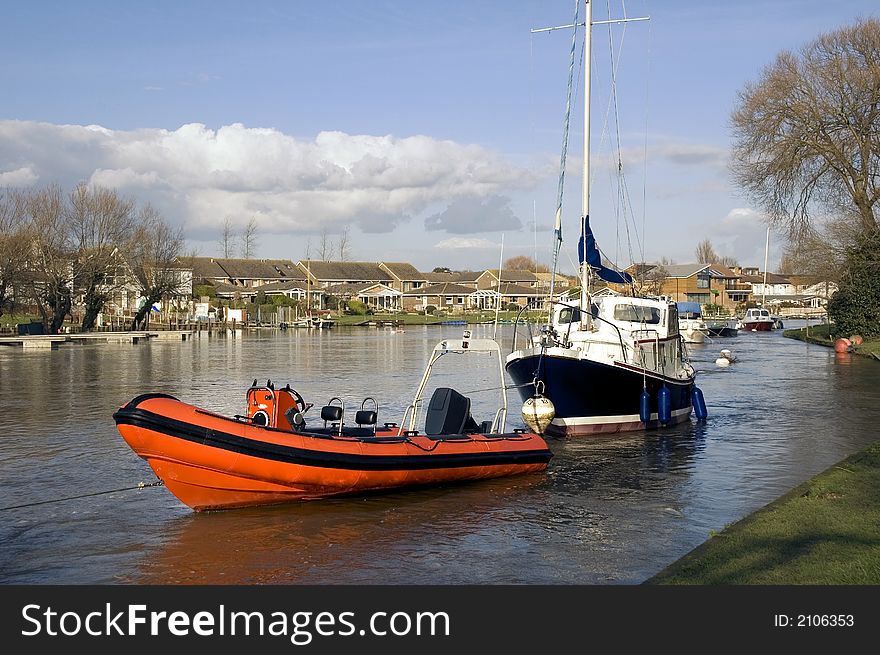 Red dinghy and boat moored on river bank on a sunny afternoon