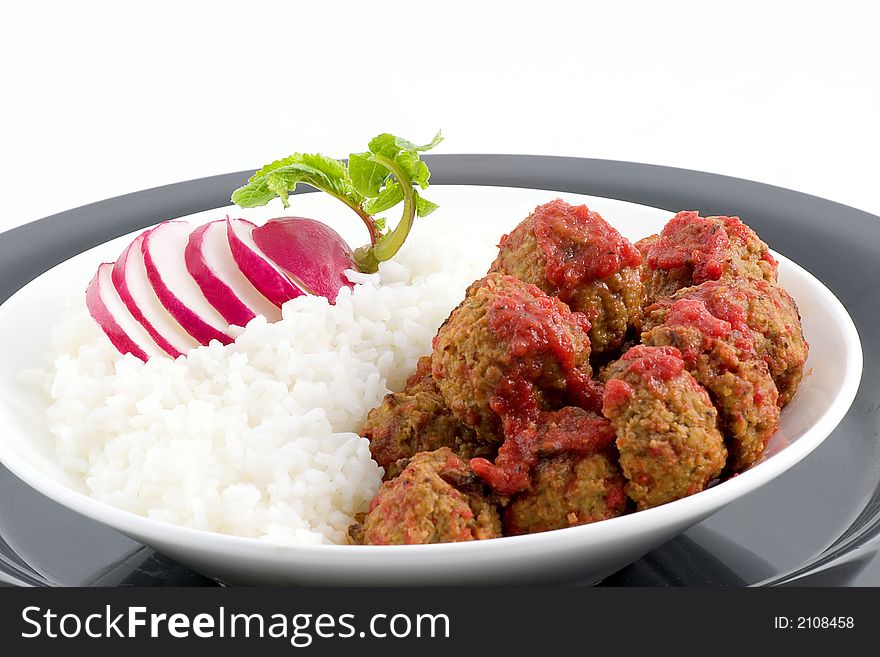 White rice plated with meat balls in a roasted pepper sauce with a docorative radish as a garnish. White rice plated with meat balls in a roasted pepper sauce with a docorative radish as a garnish.