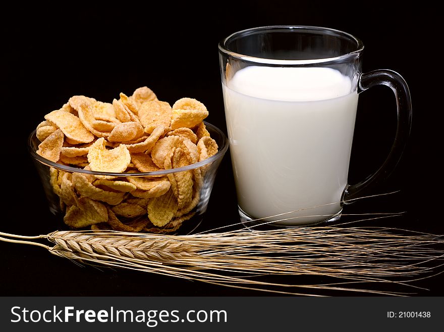 Corn flakes, glass of milk and wheat ears on a black background. Corn flakes, glass of milk and wheat ears on a black background