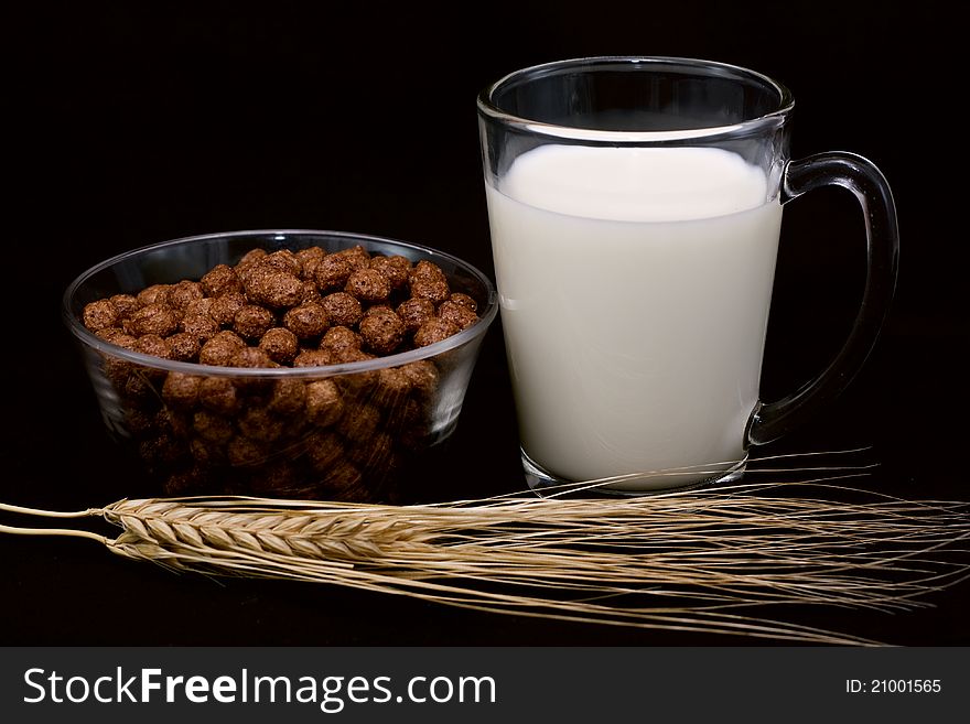 Chocolate balls, a glass of milk and wheat ears called a black background