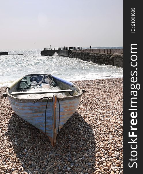 An old fishing row boat on the shore line of a pebbled beach