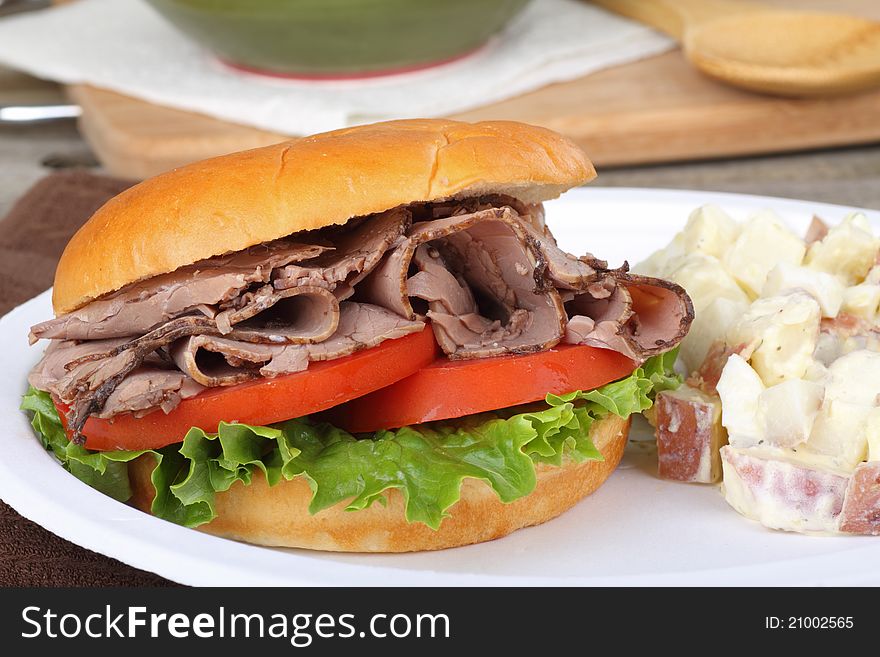 Roast beef, lettuce and tomato sandwich on a bun with potato salad