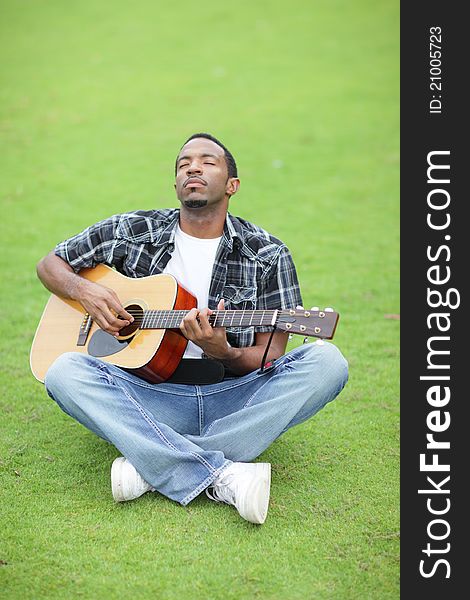 Image of a handsome young black man playing guitar in the park