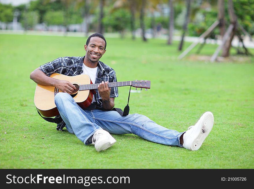 Image of a handsome young black male playing guitar in the park. Image of a handsome young black male playing guitar in the park