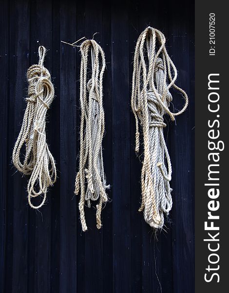 Three-strand twisted natural fibre rope hanging on black wooden wall. Three-strand twisted natural fibre rope hanging on black wooden wall.