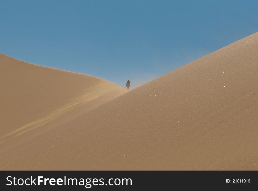 Wind blowing in high dunes in the Namib desert with a man's figure high above. Wind blowing in high dunes in the Namib desert with a man's figure high above