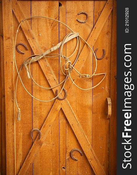 An old lasso is arranged in a decorative way with old rusted horse shoes on a golden wooden door. An old lasso is arranged in a decorative way with old rusted horse shoes on a golden wooden door