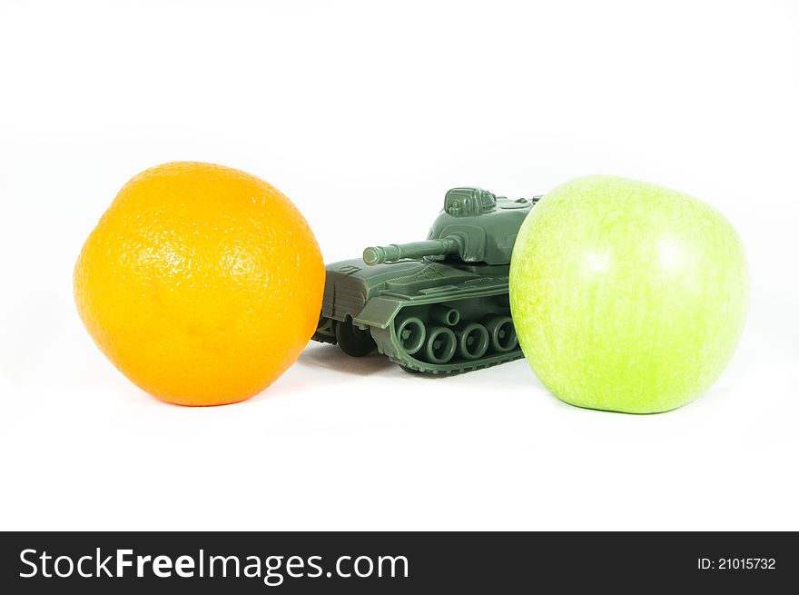 Front view of a toy tank protecting a green apple and an orange. Front view of a toy tank protecting a green apple and an orange