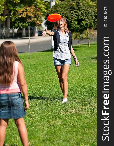 Two happy sisters playing frisbee in park outdoors