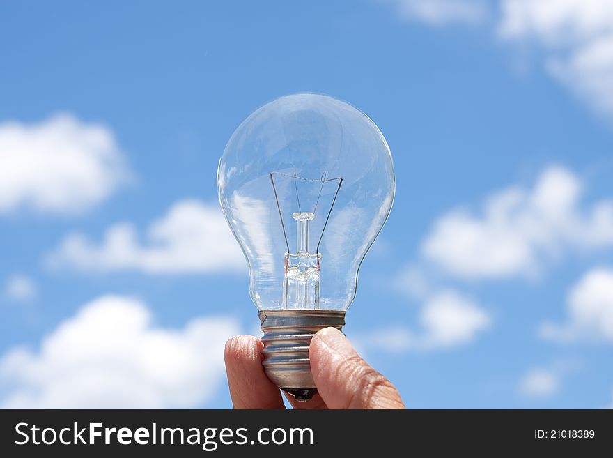 Hand holding light bulb in blue sky and cloud