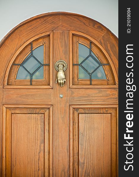 Closed wooden front door decorated with golden knocker in the form of human hand. Closed wooden front door decorated with golden knocker in the form of human hand