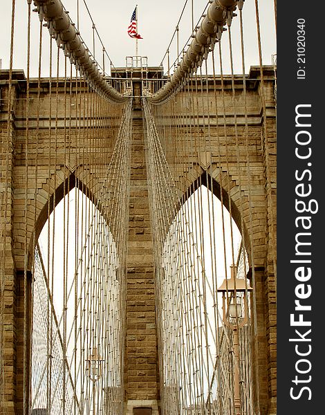 Brown toned detail photo of Brooklyn Bridge in New York City, waving American flag. Brown toned detail photo of Brooklyn Bridge in New York City, waving American flag