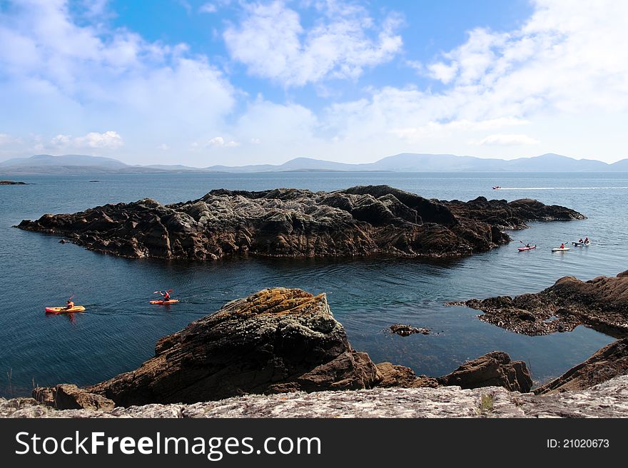 Kayaks in a scenic view in kerry ireland of rocks islands and sea with mountains against a beautiful blue cloudy sky. Kayaks in a scenic view in kerry ireland of rocks islands and sea with mountains against a beautiful blue cloudy sky