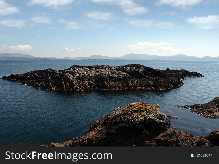 Scenic view in kerry ireland of rocks and sea with mountains against a beautiful blue cloudy sky. Scenic view in kerry ireland of rocks and sea with mountains against a beautiful blue cloudy sky