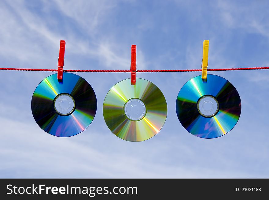 Three dvd and cd disks on clothes-line and sky. Three dvd and cd disks on clothes-line and sky