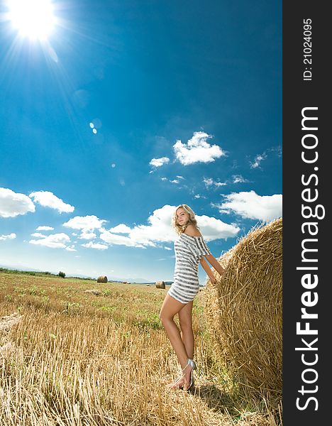 Girl at a stack of straw against a field and the sky