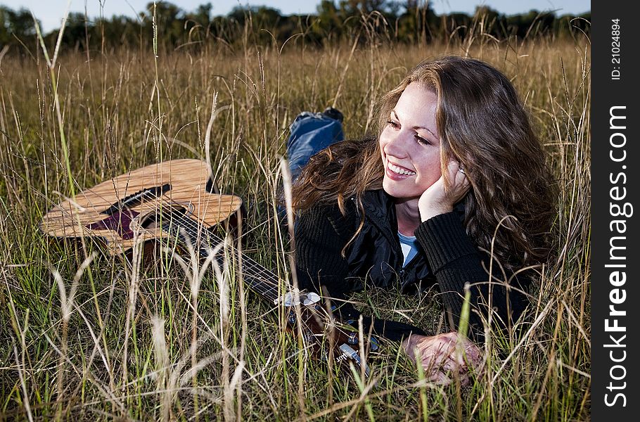 Young woman laying in field with her guitar. Young woman laying in field with her guitar
