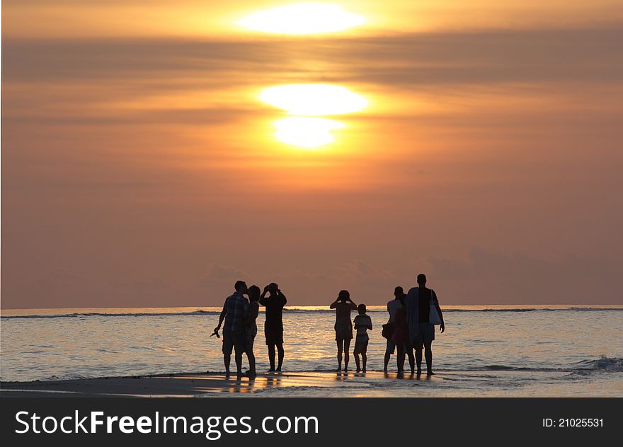 A view of a sunset in the Maldives with silhouettes of people in the distance. A view of a sunset in the Maldives with silhouettes of people in the distance.
