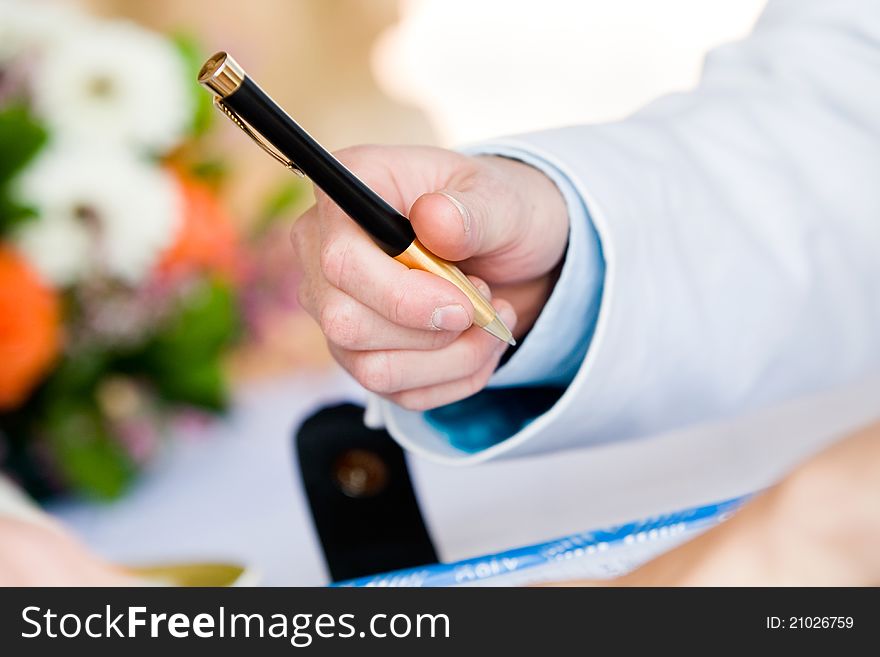 A groom holding a black and gold pen on his wedding day. A groom holding a black and gold pen on his wedding day