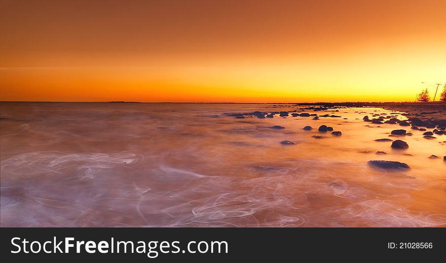 Bright red sunset over water on beach with smoke