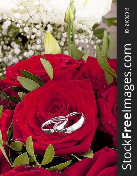 Studio-shot of white gold wedding rings on a bridal bouquet with red roses.