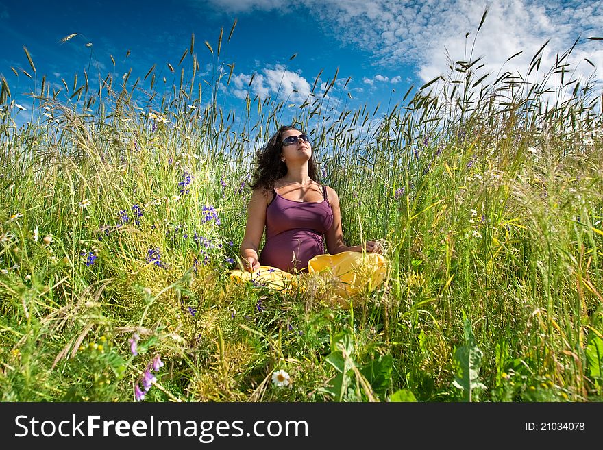 Pregnant woman on green grass field under blue sky in summer