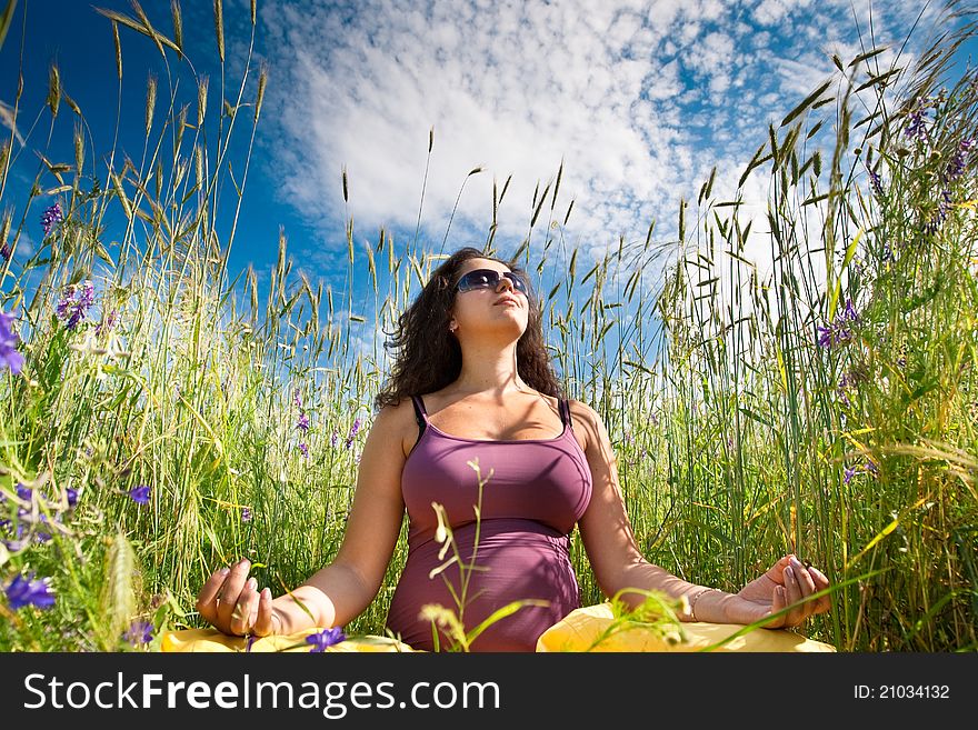 Pregnant woman on green grass field under blue sky in summer
