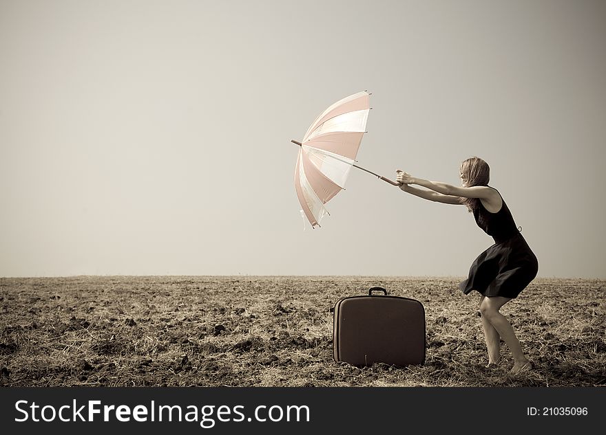 Redhead girl with umbrella at windy field. Photo in old image style.