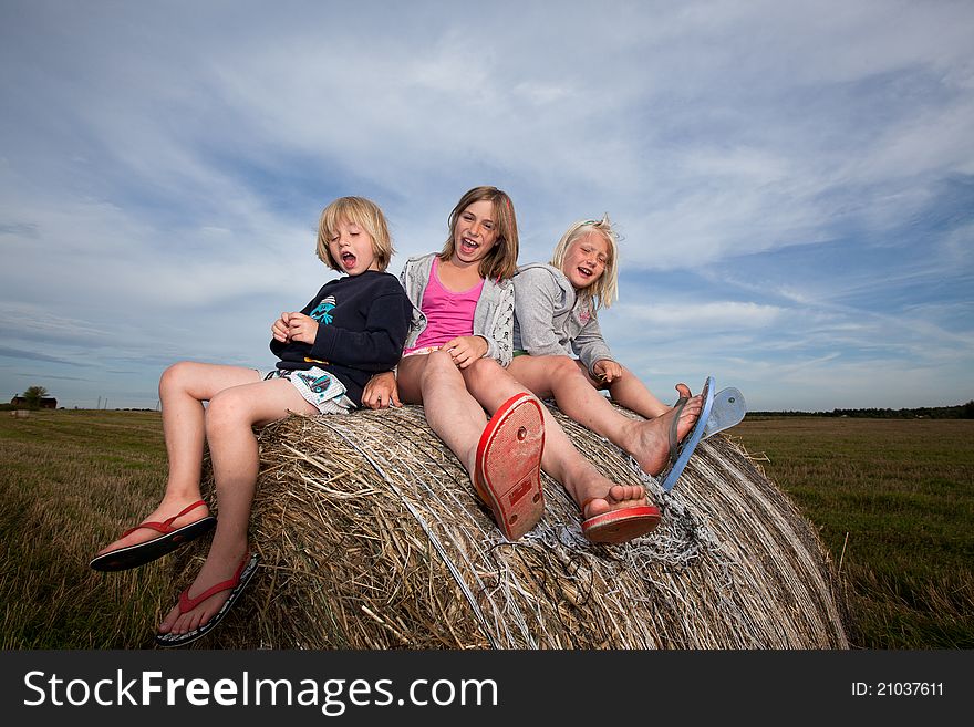 Three smilling children seated on bales of straw. Three smilling children seated on bales of straw