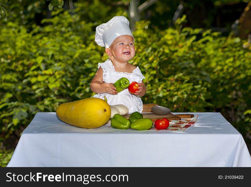 Happy little baby in cook hat with vegetables in the garden. Happy little baby in cook hat with vegetables in the garden.