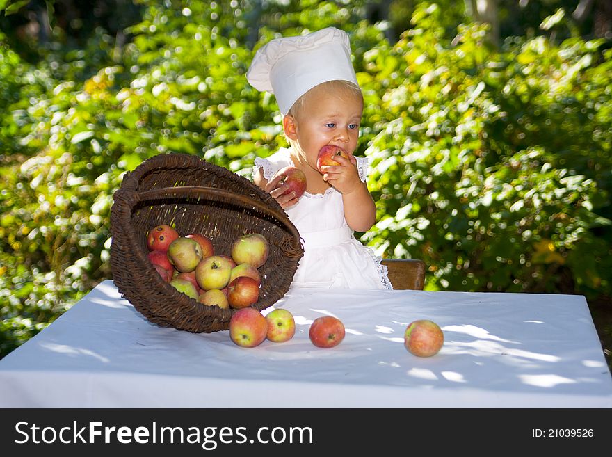 Cute small baby in cook hat and the big wicker basket of apples. Cute small baby in cook hat and the big wicker basket of apples.