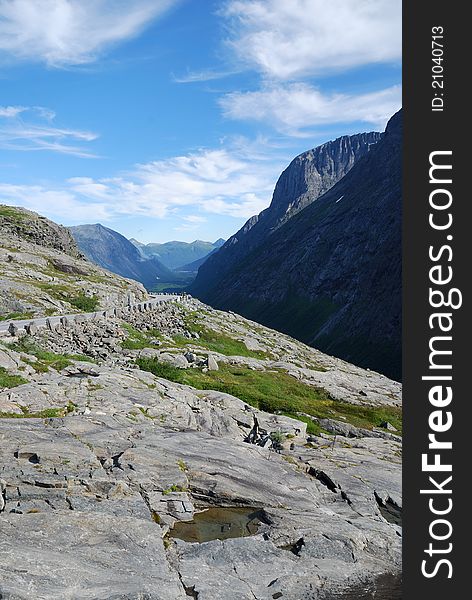 Serpentine road is meandering along the flank of mountains. Famous Trollstigen is photographed against the dark ridge of Norwegian mountains. Serpentine road is meandering along the flank of mountains. Famous Trollstigen is photographed against the dark ridge of Norwegian mountains.