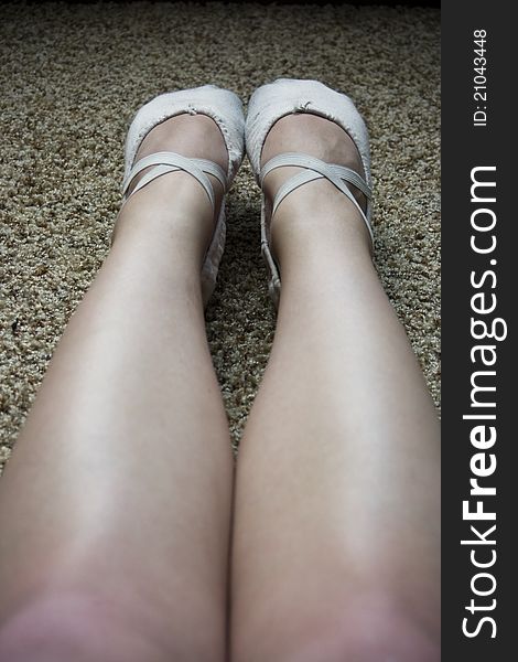 The bare outstretched legs of a ballet dancer wearing pink canvas ballet flats. The bare outstretched legs of a ballet dancer wearing pink canvas ballet flats.