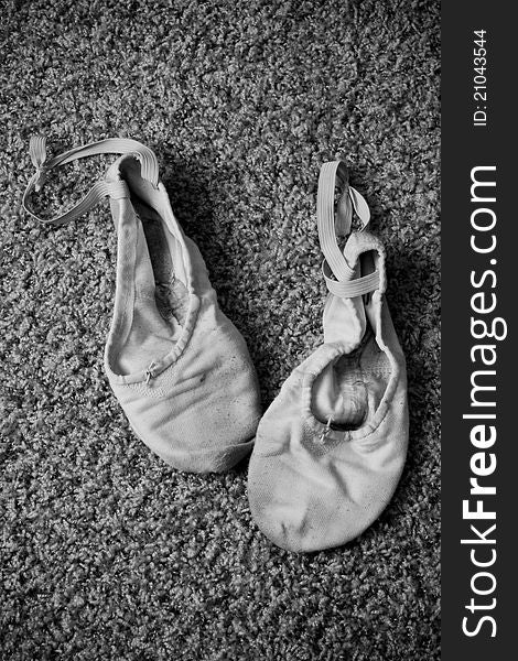 A black-and-white photo of canvas ballet slippers on carpeting.