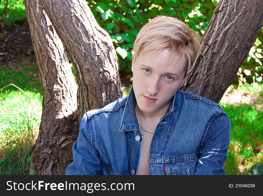 Young man in denim jacket relaxing by tree, summer scene. Young man in denim jacket relaxing by tree, summer scene.