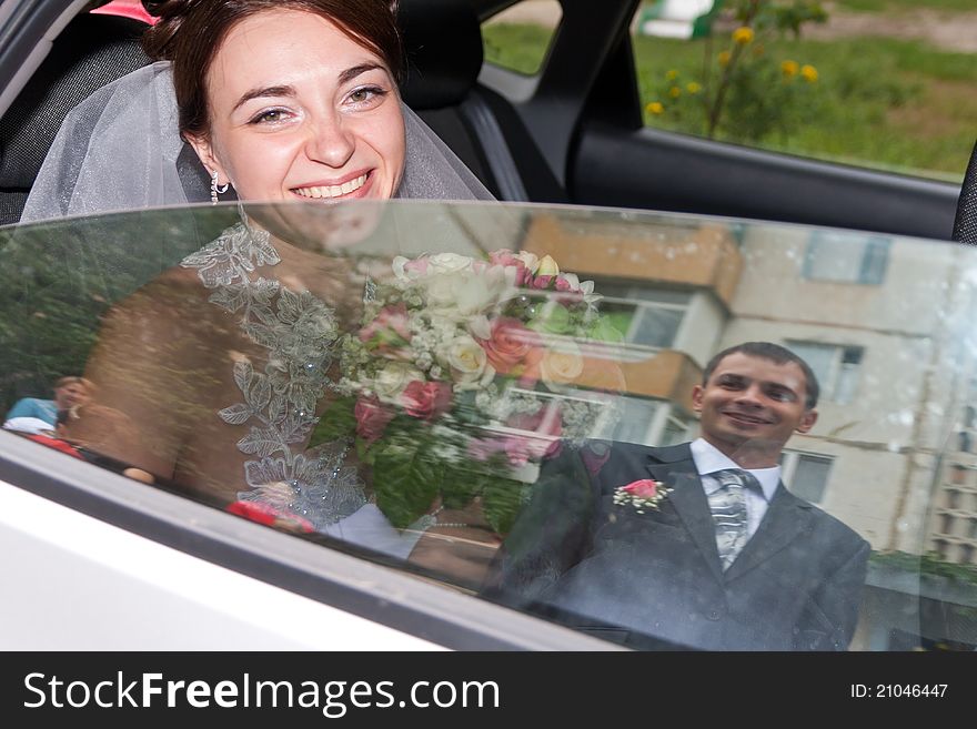 Beautiful bride looking out from car window, groom's reflection in the window