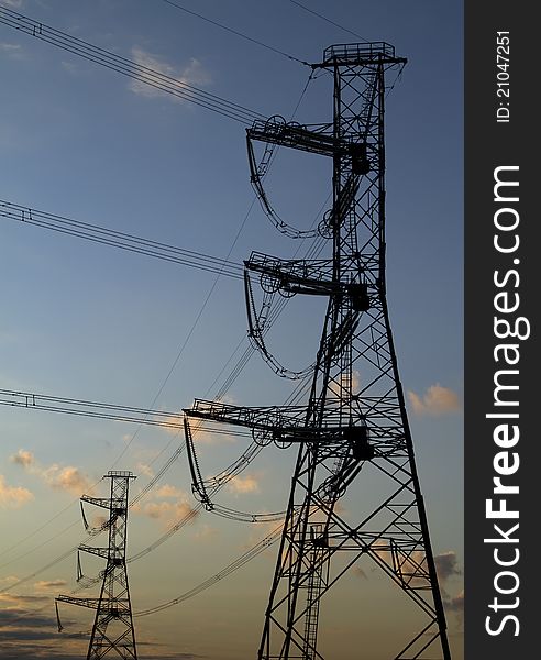 High voltage power pylons on against sunset sky