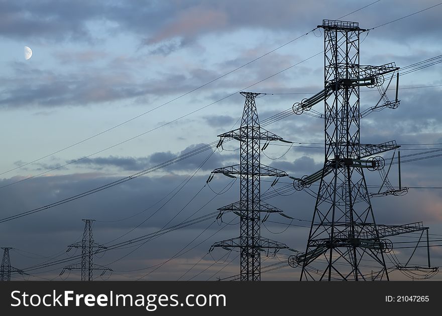 High voltage power pylons on against sunset sky, and half of the Moon. High voltage power pylons on against sunset sky, and half of the Moon